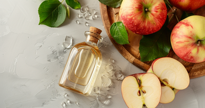 Botella de vinagre de manzana sin filtrar junto a manzanas frescas, representando un producto natural con la madre.