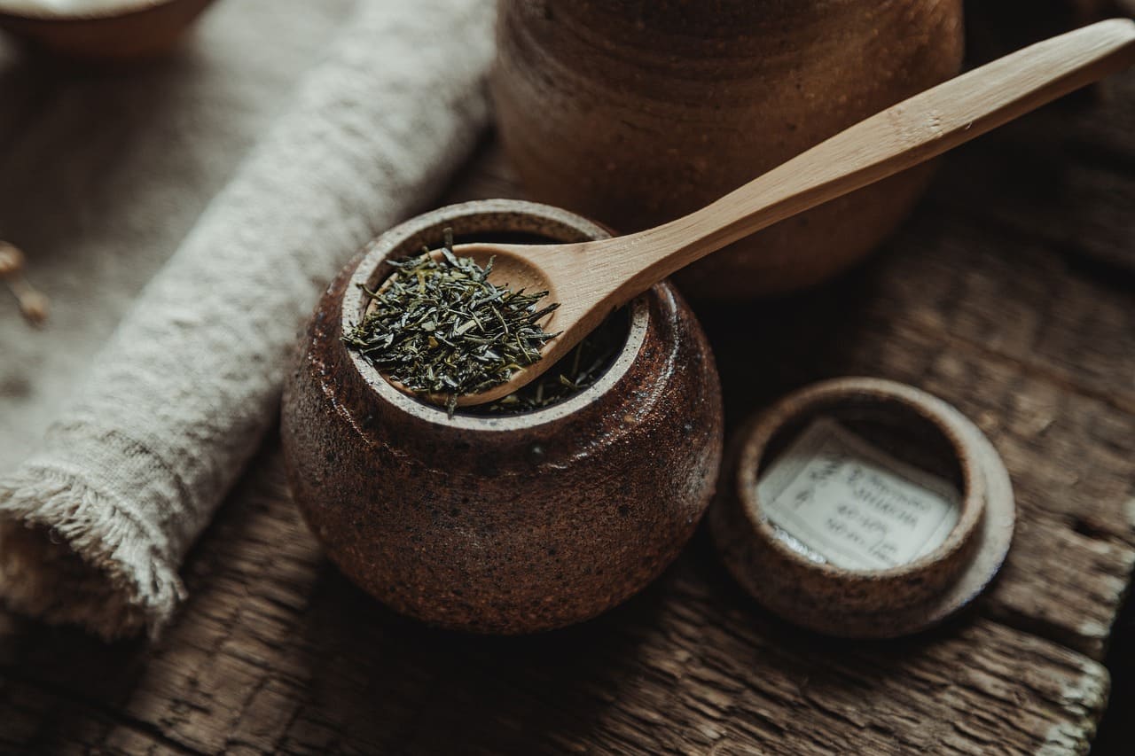 Hoja de té bancha servida en un cuenco de cerámica con cuchara de madera, imagen de estilo natural.