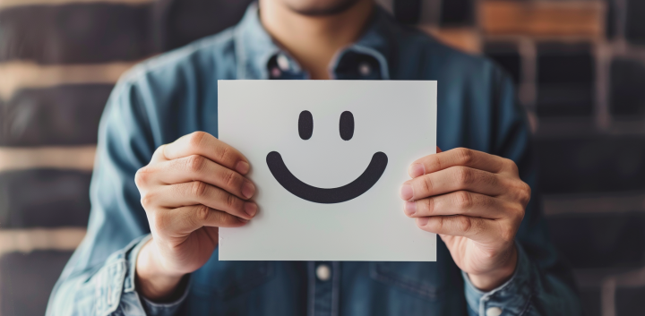 Hombre mostrando una cara sonriente en un papel como símbolo de bienestar y salud emocional.
