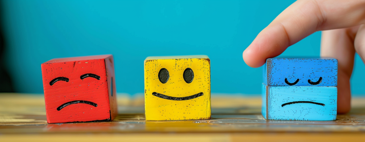 Cubos de colores con caras sonriente, neutra y triste, representando distintos estados de ánimo relacionados con la salud emocional.
