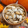 Cuenco con semillas de calabaza (pepitas) sobre mesa otoñal junto a calabazas y hojas.
