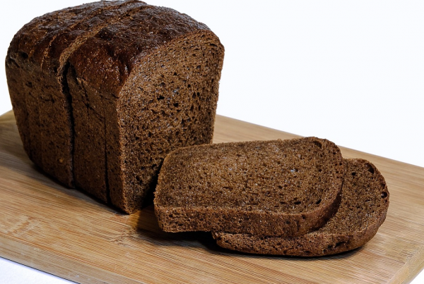 Pan de centeno integral en molde sobre tabla de madera con dos rebanadas cortadas en primer plano.