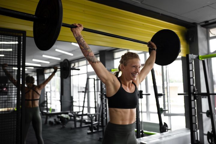Mujer realizando un levantamiento olímpico en el gimnasio, relacionado con qué comer antes y después de entrenar para optimizar el rendimiento y la recuperación.