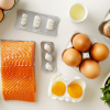 Alimentos ricos en vitamina D y nutrientes esenciales: salmón, huevos, queso, champiñones y espinacas sobre fondo claro.