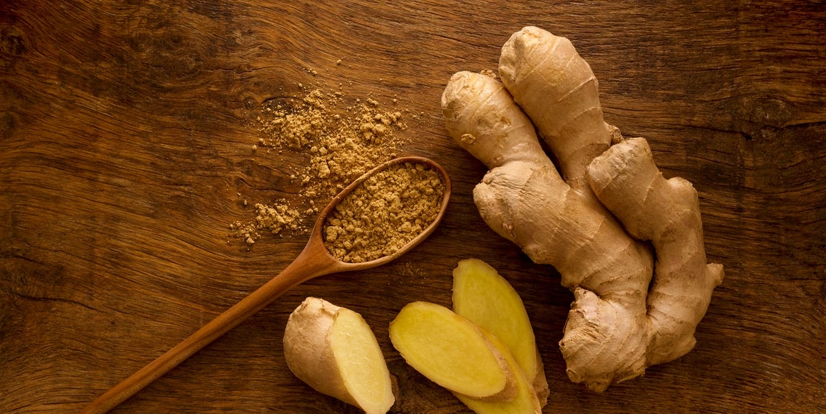 5 beneficios del jengibre: raíz fresca y rodajas sobre tabla de madera.
